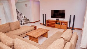 A modern living room with a beige sofa set, a wooden coffee table, and a flat-screen TV mounted on the wall. - Kilimanjaro Foothills Getaway (Marangu)