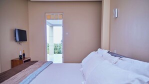 A hotel room with a bed, a television mounted on the wall, a wooden nightstand, and a door leading to a balcony. - Kilimanjaro Foothills Getaway (Marangu)