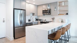 Una cocina moderna con electrodomésticos de acero inoxidable, una isla de mármol y taburetes de bar.