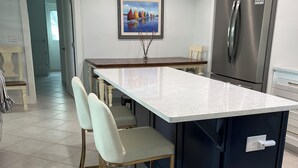 Uma cozinha moderna com ilha central, eletrodomésticos de aço inoxidável e área de refeições com duas cadeiras.
