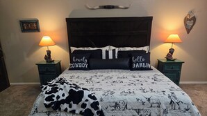 A bed with a cow print blanket, two pillows with text, a wooden headboard, and two bedside lamps. - Clean 2-bd townhome in quiet neighborhood close to all that B/CS offers. (Bryan)