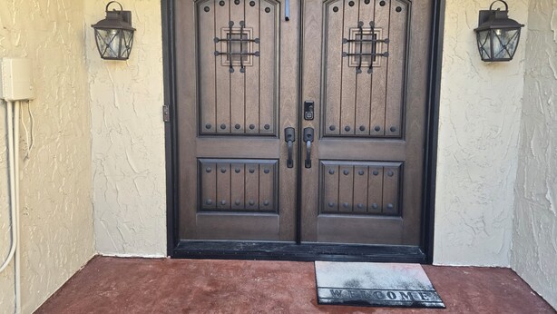 A double wooden door with a metal handle and a keyhole, flanked by two wall-mounted lanterns. - Clean 2-bd townhome in quiet neighborhood close to all that B/CS offers. (Bryan)