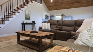 A living room with a wooden coffee table, brown leather sofa, and a staircase. - Stunning view! Hot Tub, Privacy & Relaxation (Raywick)
