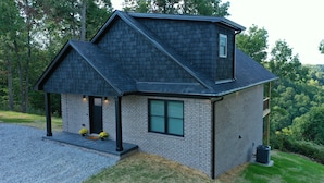 A modern two-story house with a dark shingle roof, a brick exterior, and a small porch with yellow flowers. - Stunning view! Hot Tub, Privacy & Relaxation (Raywick)