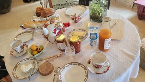 Ein Frühstückstisch mit Croissants, Brot, Marmelade, Honig, Butter und einer Orangensaftflasche.