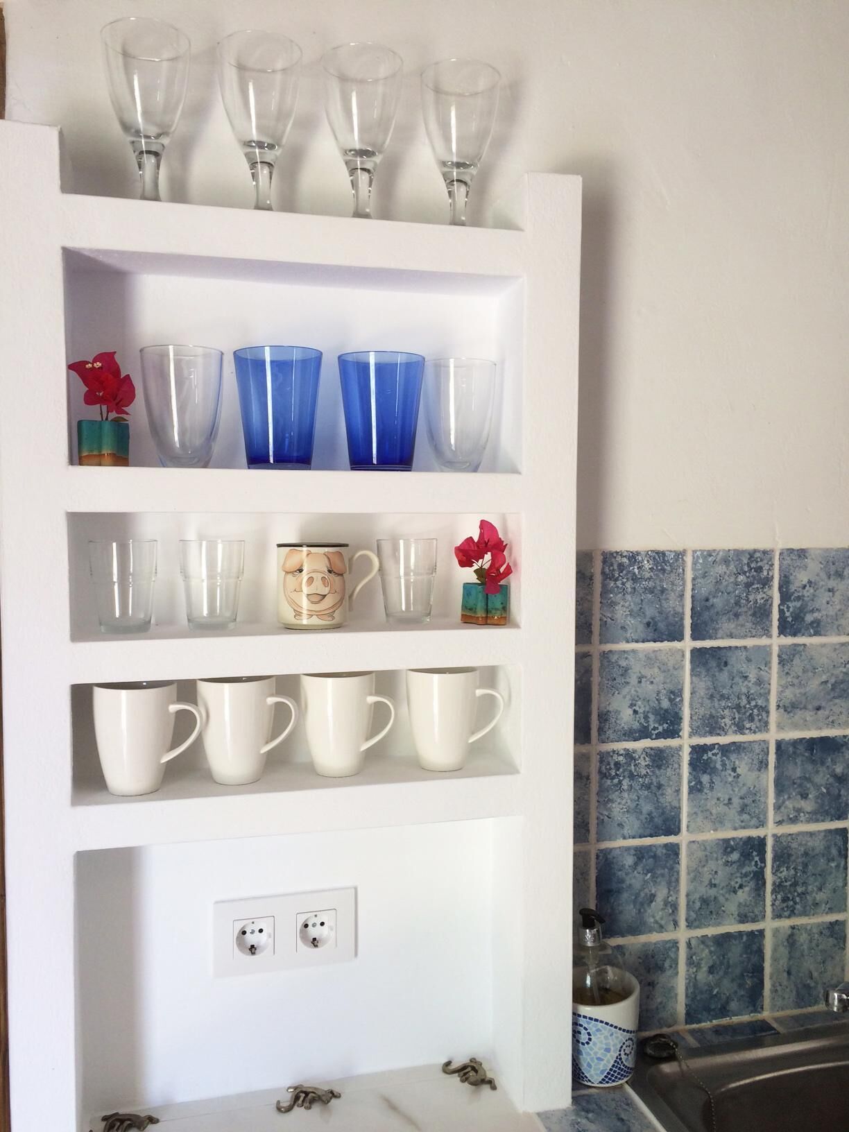A white shelf unit with various glassware and mugs.
