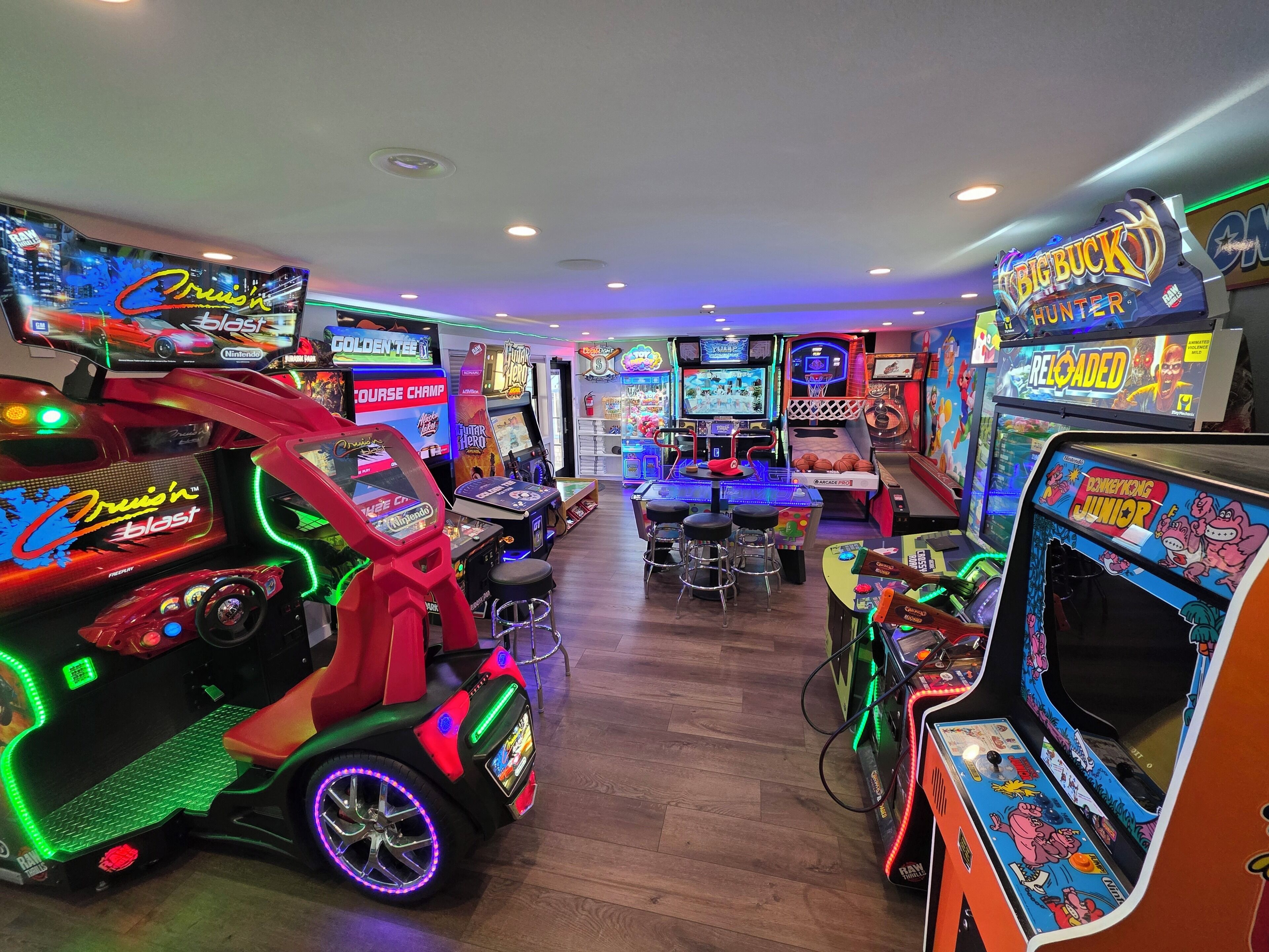 A brightly lit arcade with various gaming machines, including a racing game and a basketball game.
