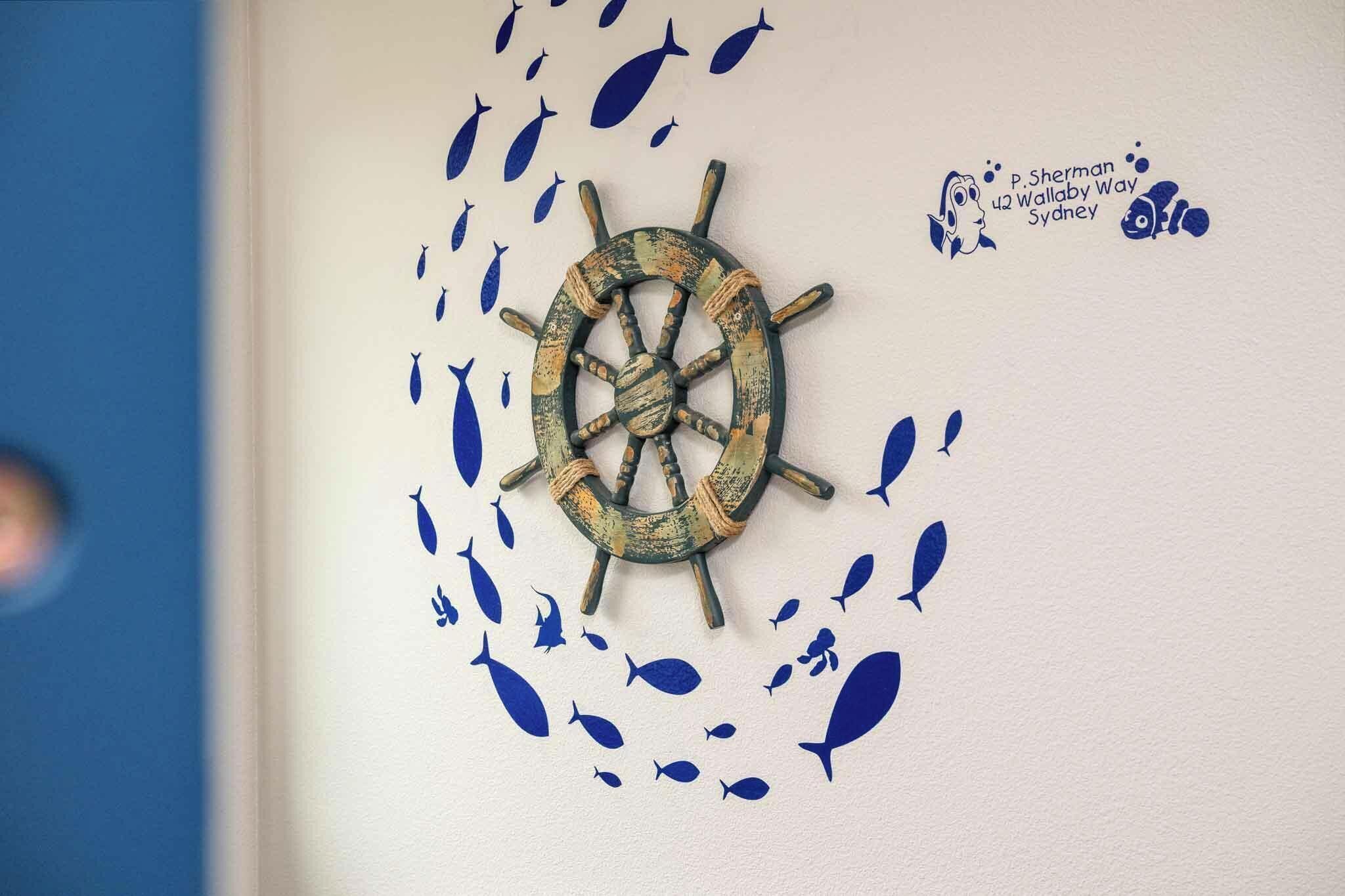 A wall with a ship's wheel and fish decals.