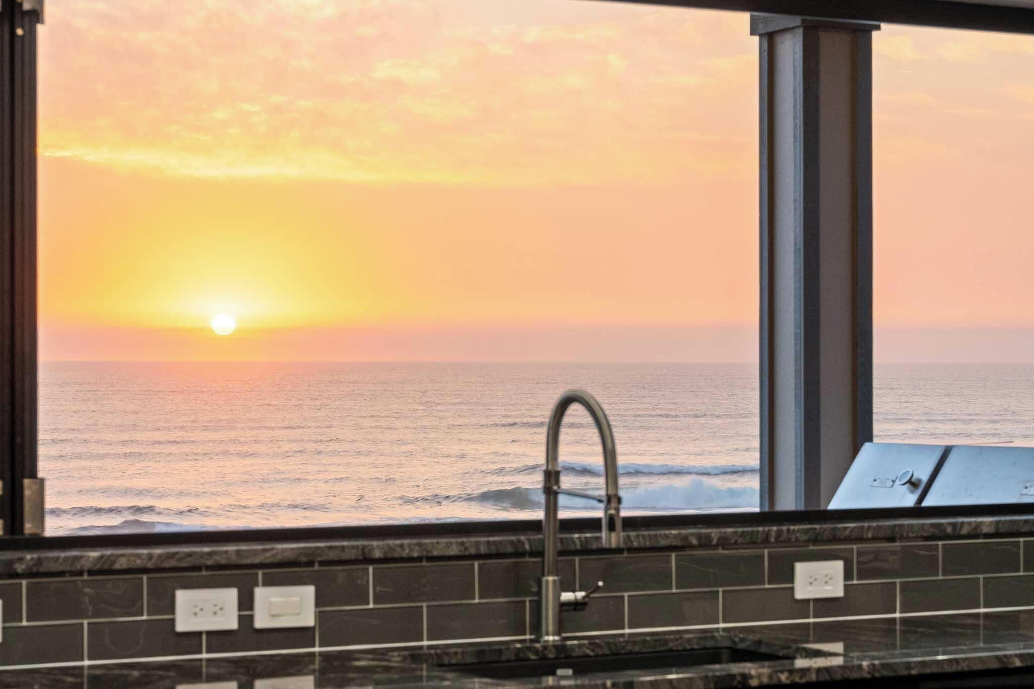 A bathroom with a view of the ocean at sunset.