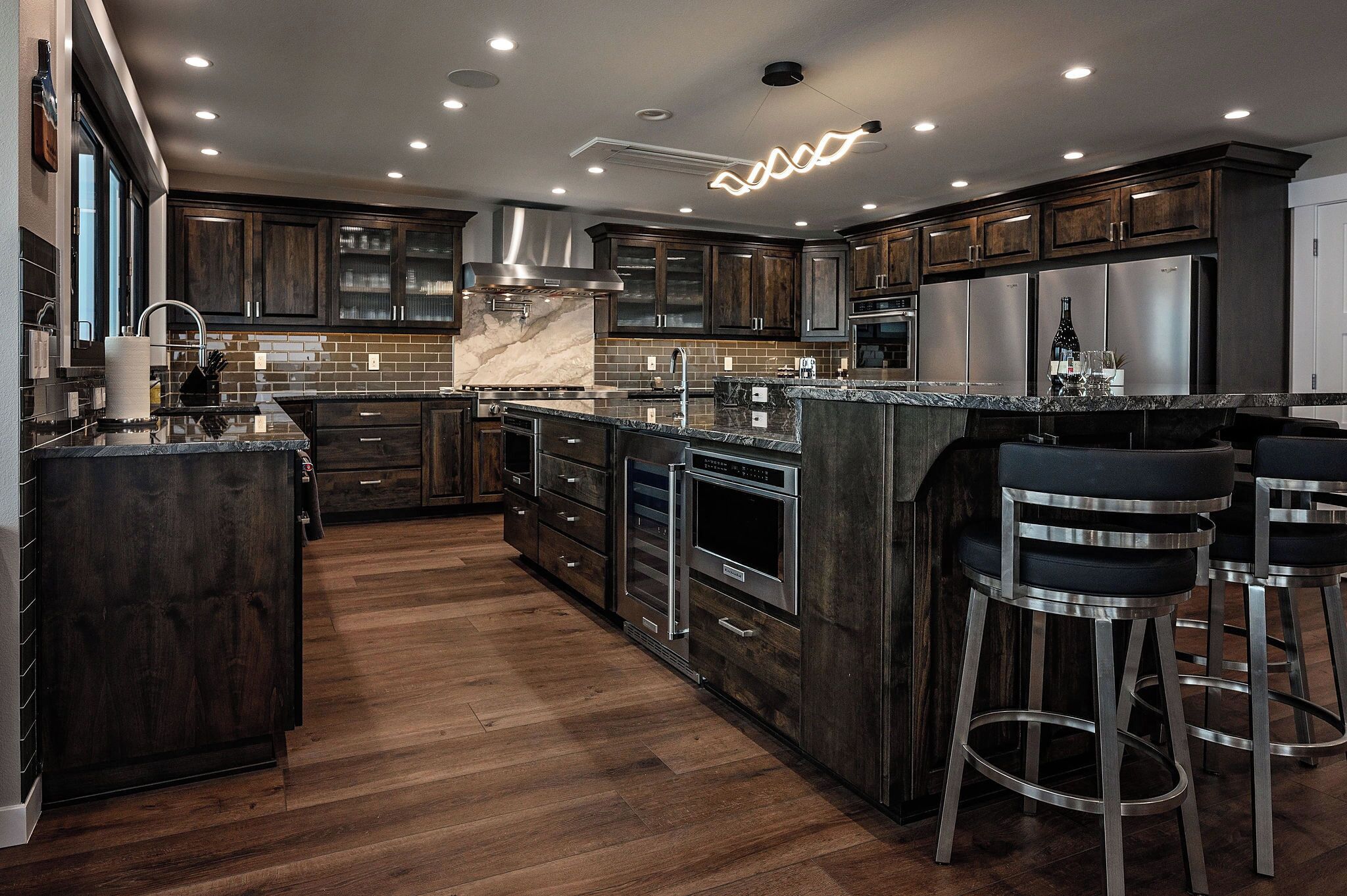 A modern kitchen with dark wood cabinets, stainless steel appliances, and a marble island.
