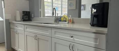 Una cocina moderna con armarios blancos, un lavamanos de acero inoxidable y una cafetera.
