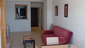 A living room with a red sofa, a wooden coffee table, and a dining table with chairs. There is a kitchen visible through a window. - Apartamento de luxe Frontal al mar (Oropesa del Mar)