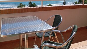 A balcony with a metal table and two wicker chairs, overlooking a beach with the ocean and a clear sky. - Apartamento de luxe Frontal al mar (Oropesa del Mar)