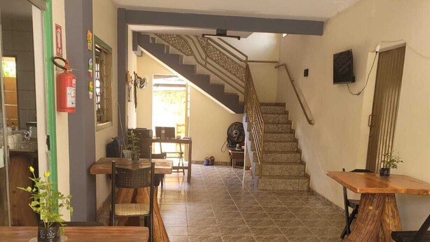 A spacious interior with a staircase leading to an upper floor, a dining area with wooden tables, and a kitchen visible in the background. - Suites Boa Viagem (Pirenópolis)