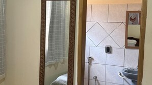 A bathroom with a toilet, sink, shower, and a television mounted on the wall. - Suites Boa Viagem (Pirenópolis)