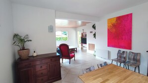 A spacious living area with a wooden dining table, a red chair, a potted plant, and a vibrant abstract painting on the wall. - This house is no longer available for rent (Moliets-et-Maa)