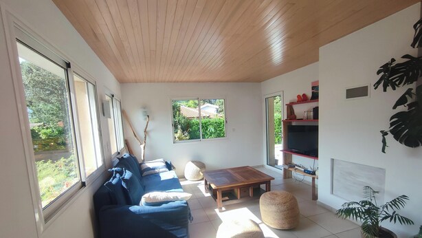 A modern living room with a wooden ceiling, a blue sofa, a wooden coffee table, and a TV on a shelf. - This house is no longer available for rent (Moliets-et-Maa)