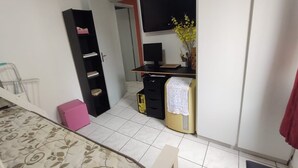 A bedroom with a bed, a desk with a computer, a wardrobe, and a small pink storage box.