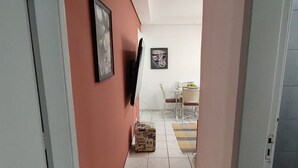 A narrow hallway with a tiled floor, a television mounted on the wall, and a dining area in the distance.