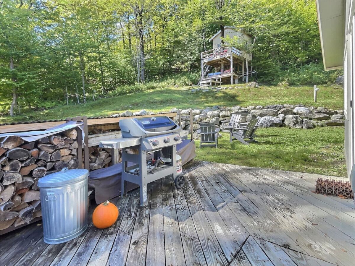 A wooden deck with a grill, a trash can, and a pumpkin.