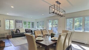 Un salon spacieux comprenant un coin repas, de grandes fenêtres et un lustre moderne.