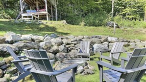 Un espace extérieur aménagé dans un style rustique, avec des fauteuils Adirondack et une table en métal, entouré d’un mur de pierres et d’une terrasse en bois.