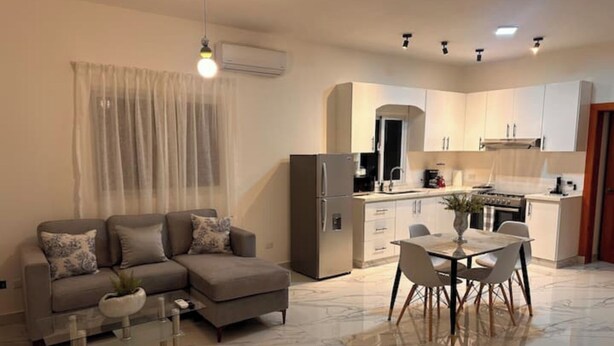 A modern living room with a sofa, a glass coffee table, and a dining area with a table and chairs. - Apartamento 1BED sosua 1minute from airport pop (Puerto Plata)