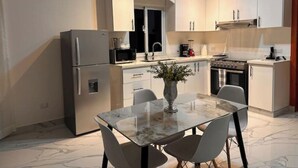 A modern kitchen with white cabinets, a stainless steel refrigerator, a microwave, and a stove. There is a dining table with chairs and a vase with flowers. - Apartamento 1BED sosua 1minute from airport pop (Puerto Plata)