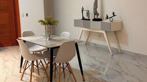 A dining area with a marble table, white chairs, a vase with green plants, and a console table with sculptures. - Apartamento 1BED sosua 1minute from airport pop (Puerto Plata)
