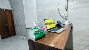 Ett skrivbord i trä med en bärbar dator som visar texten ”ARSAKHA” och en grön plastpåse.