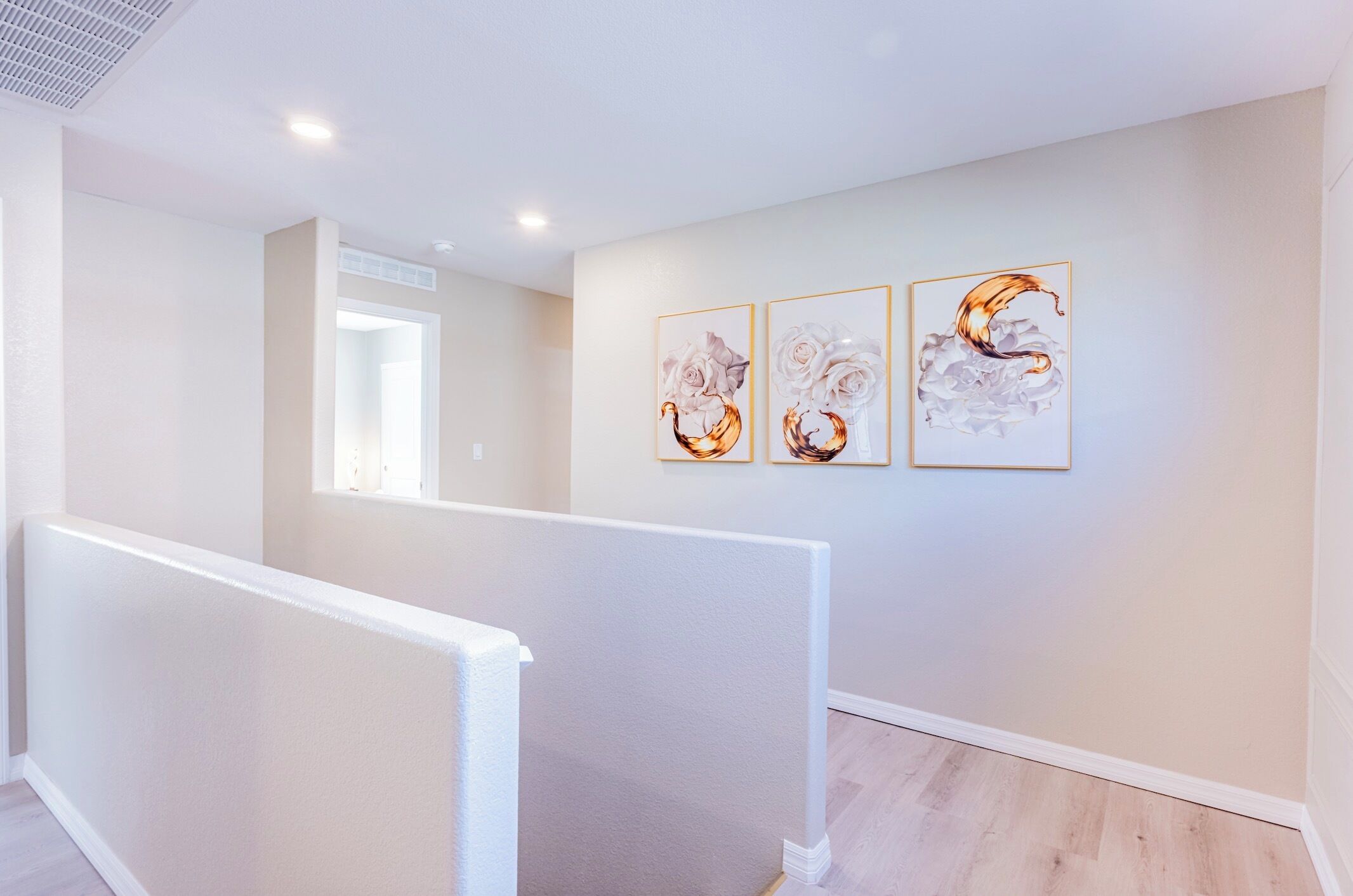 A modern interior with a wooden floor, white walls, and a staircase. There are three framed artworks on the wall.