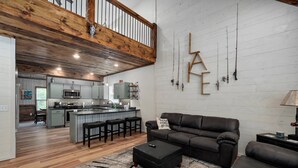 Un amplio salón con un sofá de cuero oscuro, una mesa de centro y una cocina al fondo.