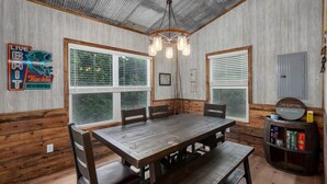 Un comedor rústico de madera con una mesa grande y bancos, una araña y una estantería llena de libros.