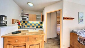 Een kleine keuken met een magnetron, fornuis en spoelbak. Er is een zithoekje met een tafel en stoelen.