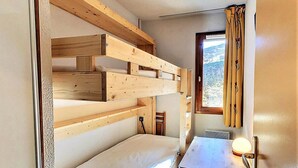 Een kleine kamer met stapelbedden, een tafeltje en een raam met gordijnen.
