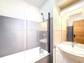 Een badkamer met een douche, wastafel en spiegel.