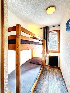 Een kleine, compacte kamer met een stapelbed, een raam met uitzicht en een plafondlamp.