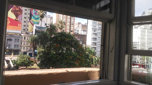 A view from a window with a building in the background, a tree in the foreground, and a clear sky.