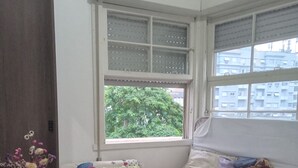 A cozy room with a bed, a small table, and a window with a view of buildings and trees.