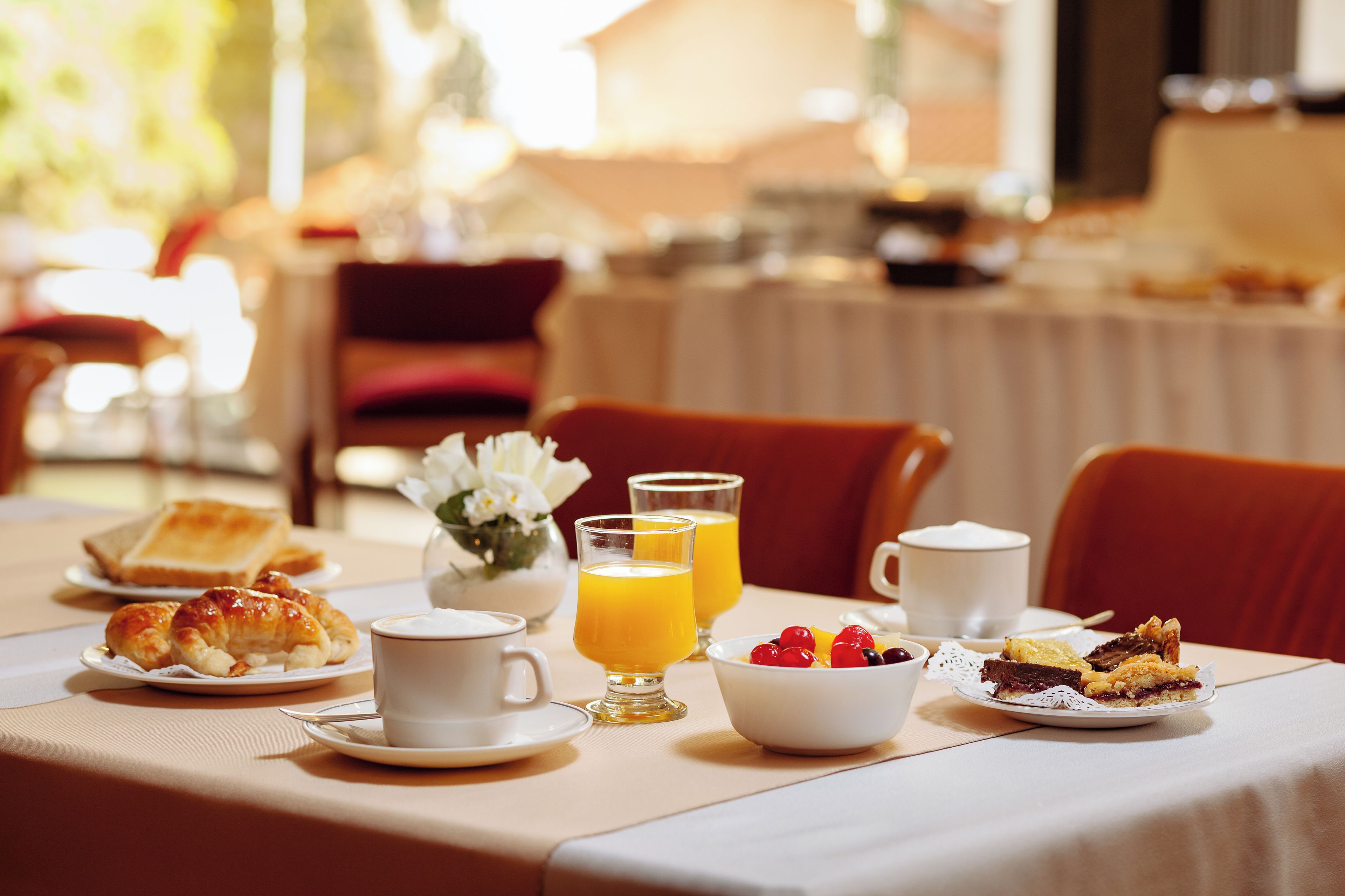 A breakfast table with croissants, coffee, juice, and fruit.