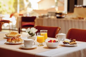 Una mesa de desayuno con croissants, café, jugo y fruta.