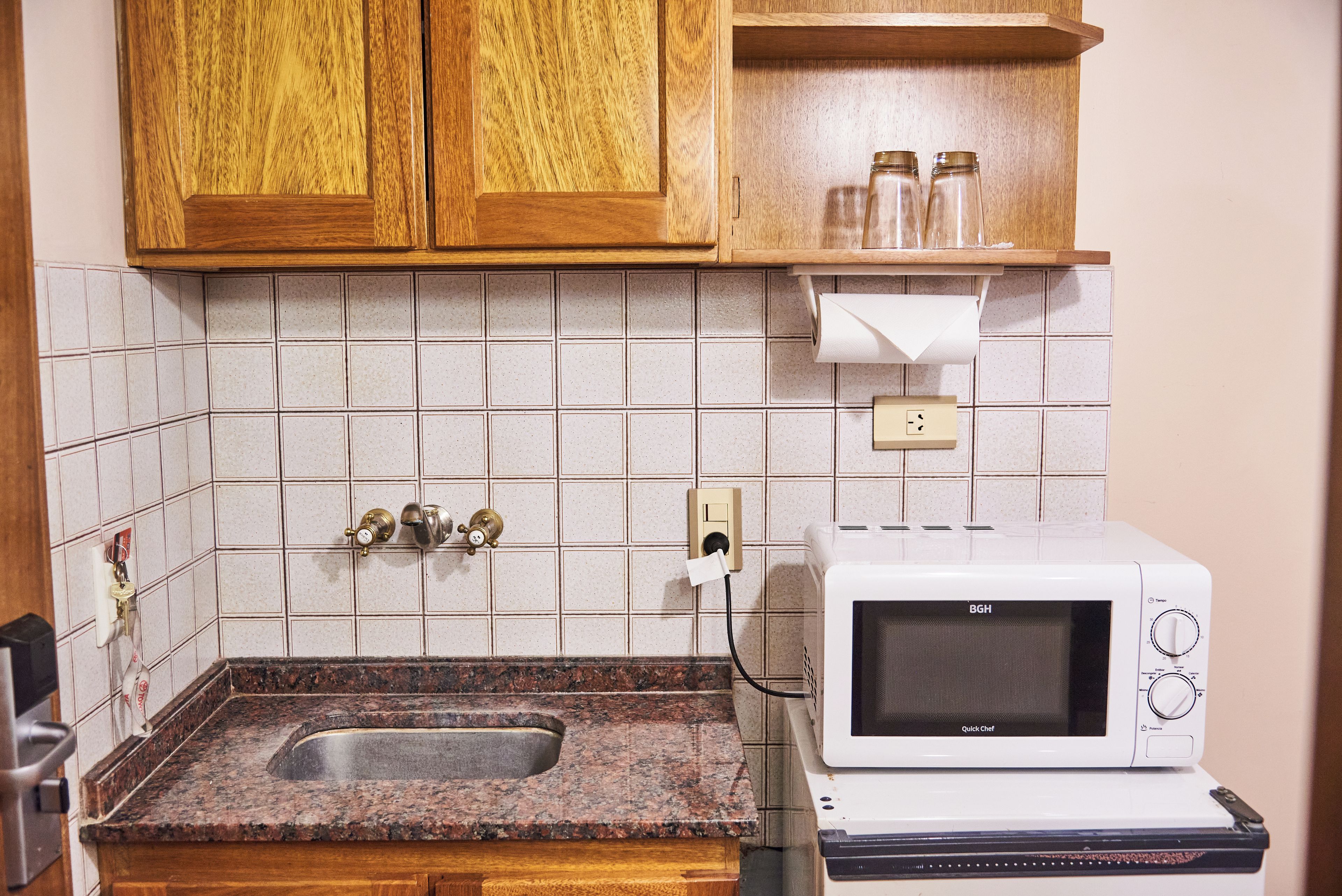 A kitchen with a granite countertop, a microwave, a sink, wooden cabinets, and a tiled backsplash.