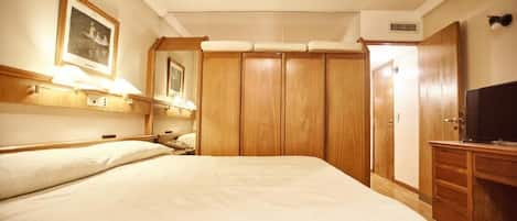 Habitación de hotel con una cama grande, armario de madera y televisor sobre un mueble de madera.