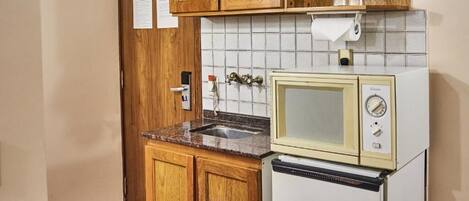 Una cocina compacta con armarios de madera, un microondas integrado y un lavamanos.