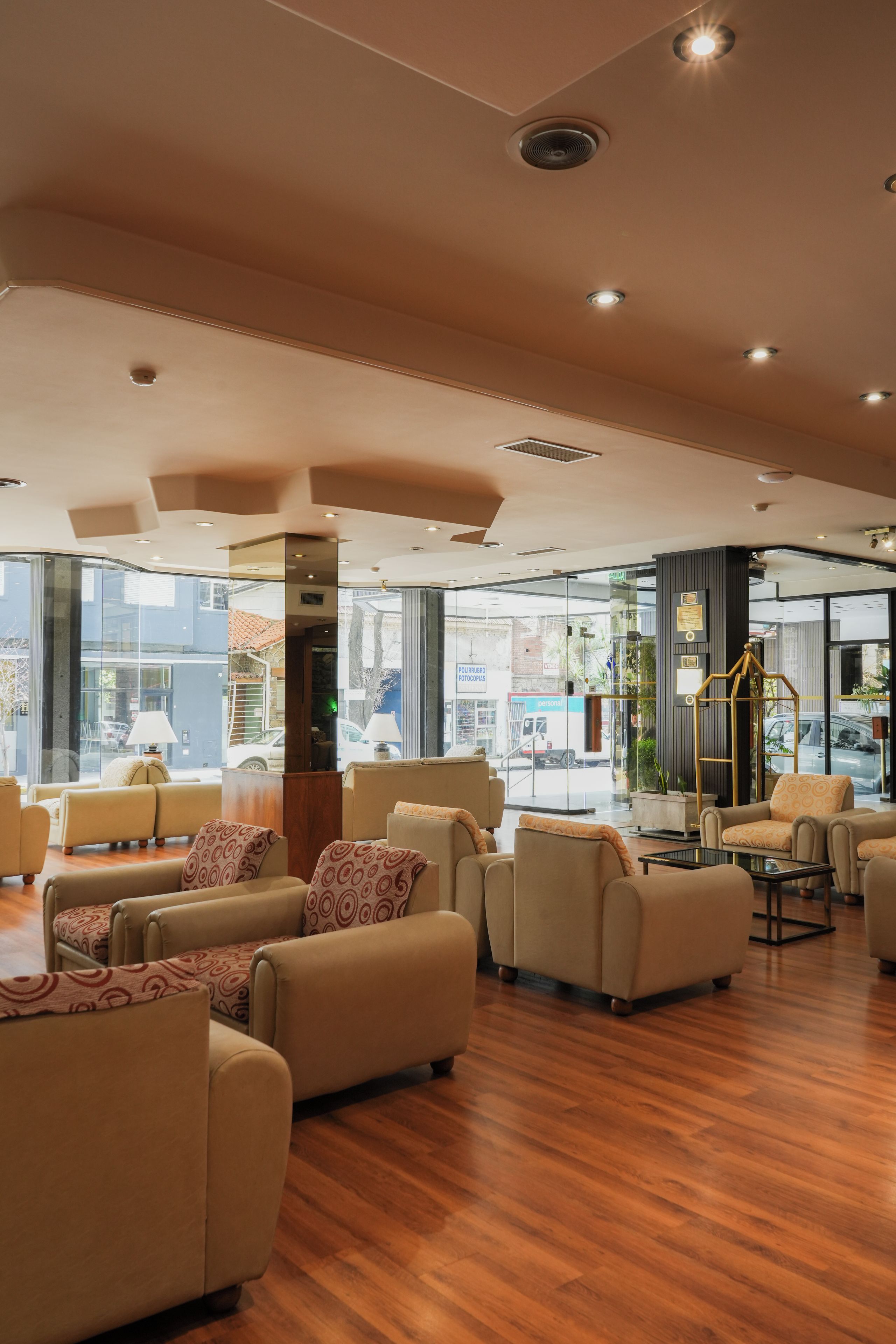 A hotel lobby with multiple seating areas, a reception desk, and large windows offering views of the street.