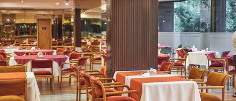 A restaurant with multiple tables and chairs, wooden flooring, and large windows allowing natural light.