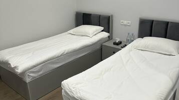 A room with two single beds, a bedside table with a lamp, and a wall-mounted air conditioner.