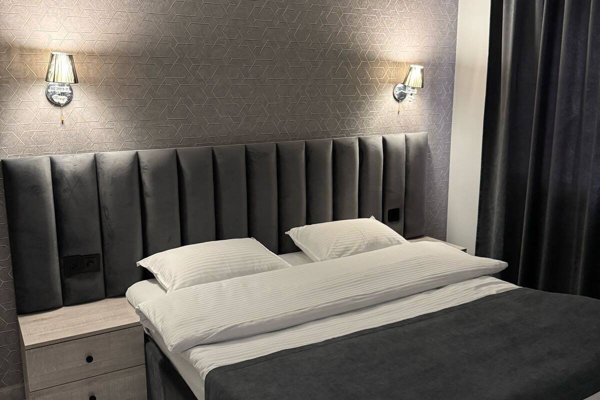 Un dormitorio moderno con pared de estampado geométrico, cabecera acolchada, mesita de noche con cajones y una cama grande con ropa de cama blanca.