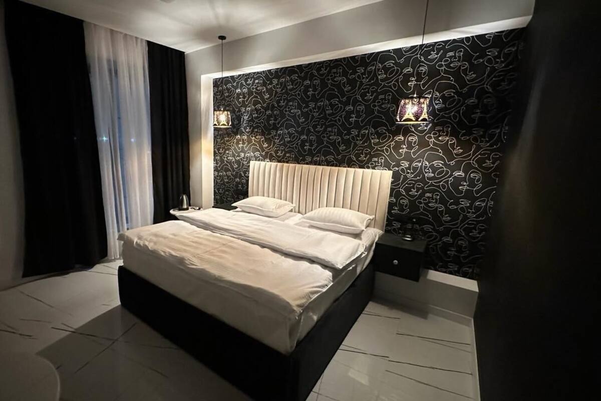 Un dormitorio moderno con una cama grande, un papel tapiz estampado y una mesita de noche con una lámpara.
