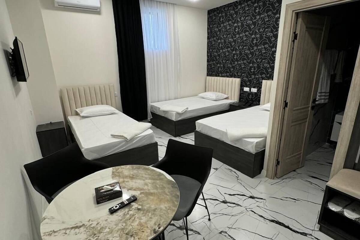 Habitación de hotel con dos camas individuales, una pequeña mesa con sillas, piso estampado tipo mármol y pared con diseño blanco y negro.